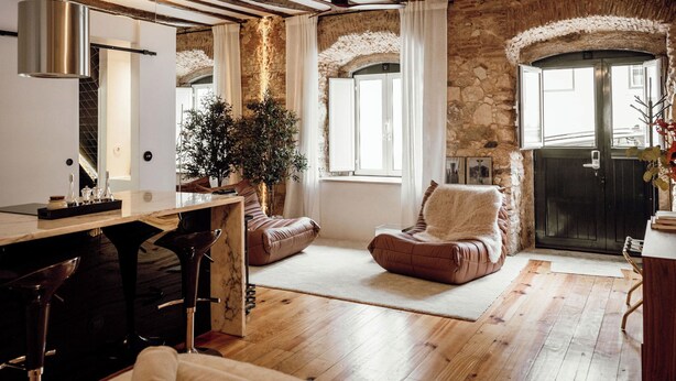 Ein rustikales Interieur mit freiliegenden Holzbalken, Steinwänden, einer großen Topfpflanze und einer gemütlichen Sitzecke mit Kamin.