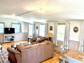 Ein Wohnzimmer mit Sofa, Fernseher und einem Essbereich mit Tisch und Stühlen.