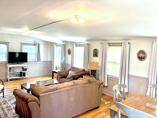Uma sala de estar com sofá, televisão e uma área de jantar com mesa e cadeiras.