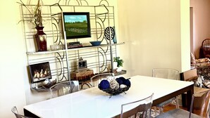Een eetruimte met een witte tafel, transparante stoelen, een decoratieve wandkast en een kamerbreed tapijt.