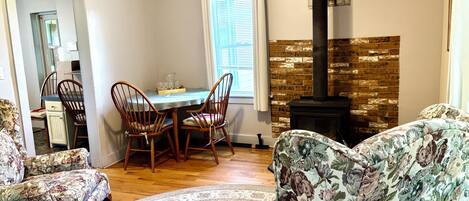 Una sala de estar con chimenea, sillas de estampado floral, una mesa de comedor y una alfombra.