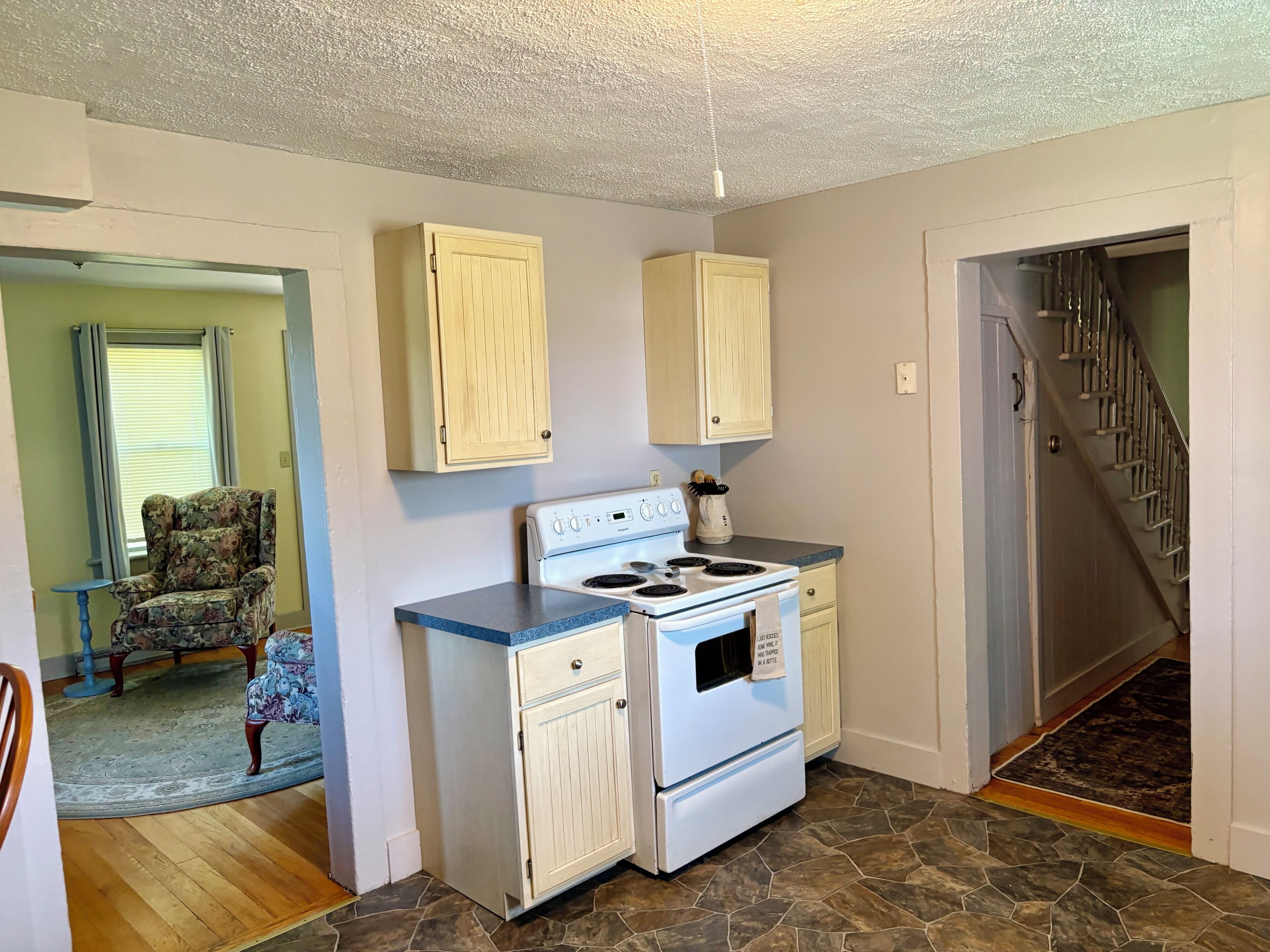 A kitchen with a stove, cabinets, and a dining area with a chair and table.