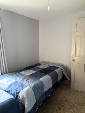 A single bed with a blue and white quilt in a room with light gray walls and a closed door. - Farmhouse in Gardiner (Gardiner)