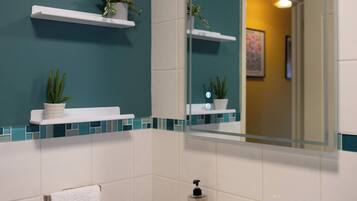 Een badkamer met een witte wastafel, wanden in turquoise en witte tegels. Er zijn twee witte planken met potplanten.