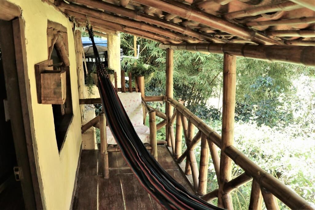 A wooden deck with a hammock, bamboo railing, and a view of greenery.