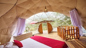 Eine Zelthotelunterkunft mit einem Bett, Holzmöbeln und Blick durch einen großen Bogen.
