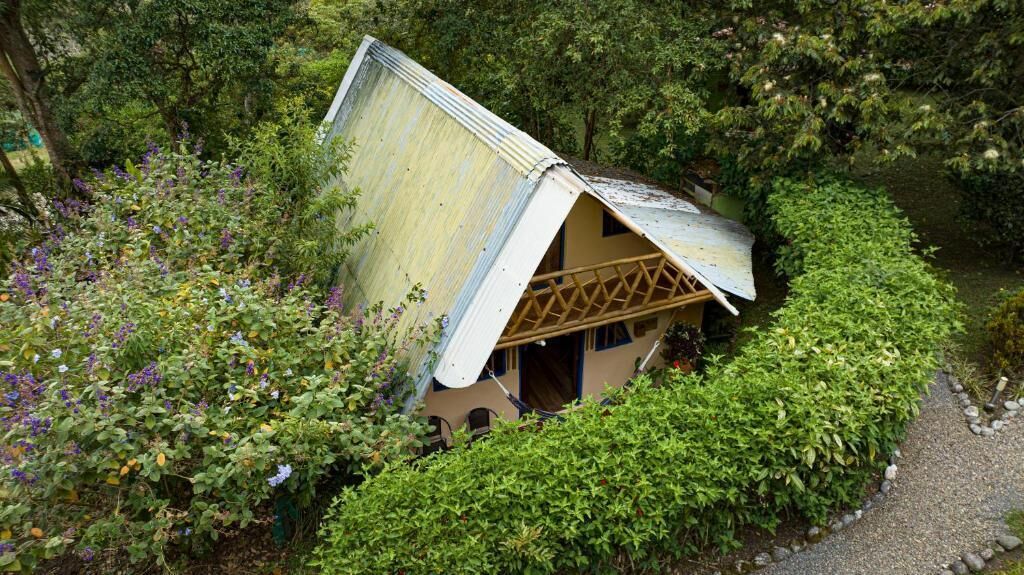 Ein kleines, rustikales Haus, eingebettet in einen üppigen Garten, mit einem geneigten Dach und einer Holzlattung.
