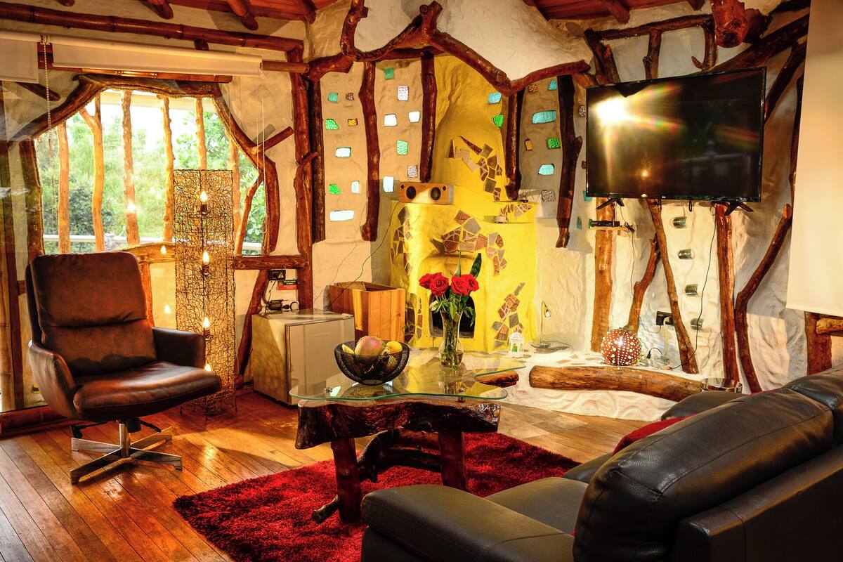 Un salon chaleureux avec un plafond en bois, un téléviseur fixé au mur, un confortable canapé en cuir, une table basse en verre et un tapis rouge.