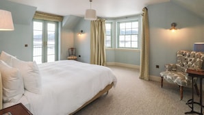 A bedroom with a large bed, two windows with curtains, a chair, and a lamp. - Schiehallion House (Pitlochry)