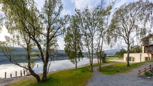 A lakeside property with a gravel path, trees, and a building with a balcony overlooking the water. - Schiehallion House (Pitlochry)