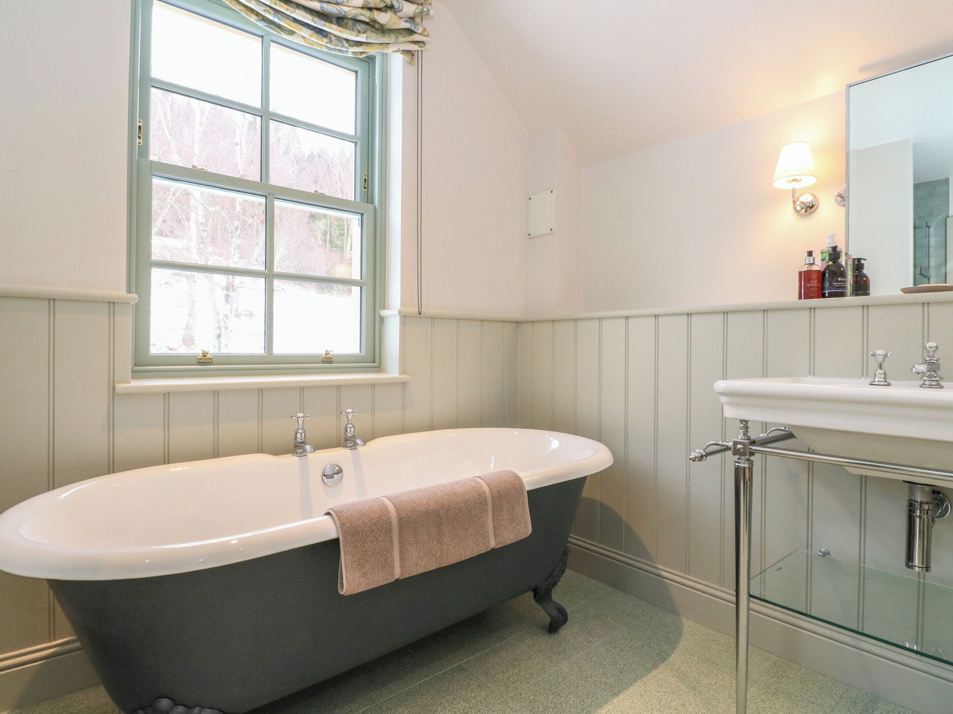 A bathroom with a freestanding bathtub, a vanity with a mirror, and a window with curtains.