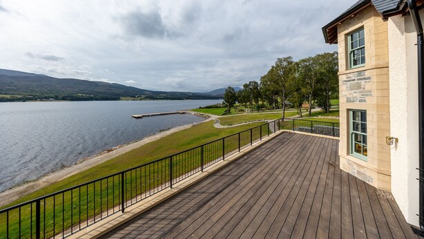 A lakeside property with a wooden deck, stone building, and a view of the lake and hills. - Schiehallion House (Pitlochry)