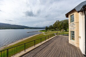 Ein Seeufergrundstück mit Holzterrasse, Steinhaus und Blick auf See und Hügel.