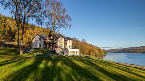 A large house with multiple sections, a well-maintained lawn, and a lake in the background. - Schiehallion House (Pitlochry)