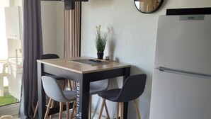 A modern kitchen with a wooden table, two chairs, a refrigerator, a clock, and a potted plant. - Cosy seaside studio in Jard-sur-Mer - Beach 50 m away, private parking (Jard-sur-Mer)