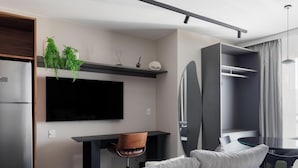 Ett modernt hotellrum med en platt-TV, en soffa, ett matbord och en inbyggd garderob.