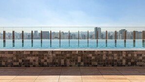 A rooftop infinity pool with a cityscape view, tiled floor, and clear sky. - DOru Vila Nova Conceição by Wecare (São Paulo)