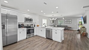 A modern kitchen with white cabinetry, stainless steel appliances, and a wooden floor. - 2Luxe Beach Homes• Beach• Pool,Spa,HotTub,Firepit (Saint Augustine)