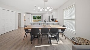 A modern dining area with a wooden table, black chairs, and a chandelier. - 2Luxe Beach Homes• Beach• Pool,Spa,HotTub,Firepit (Saint Augustine)