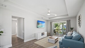 A modern living room with a blue sofa, a coffee table, and a TV on the wall. - 2Luxe Beach Homes• Beach• Pool,Spa,HotTub,Firepit (Saint Augustine)