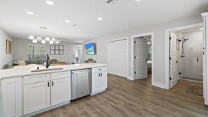 A modern kitchen with white cabinetry, a central island, and a built-in dishwasher. - 2Luxe Beach Homes• Beach• Pool,Spa,HotTub,Firepit (Saint Augustine)