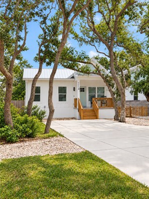 A single-story house with a white exterior, a front porch with a wooden railing, and a clear sky.