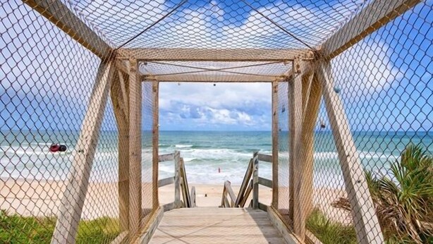 A beach view through a wooden structure with a netted roof, leading to a sandy beach. - Brand New Immaculate Cottage (Saint Augustine)