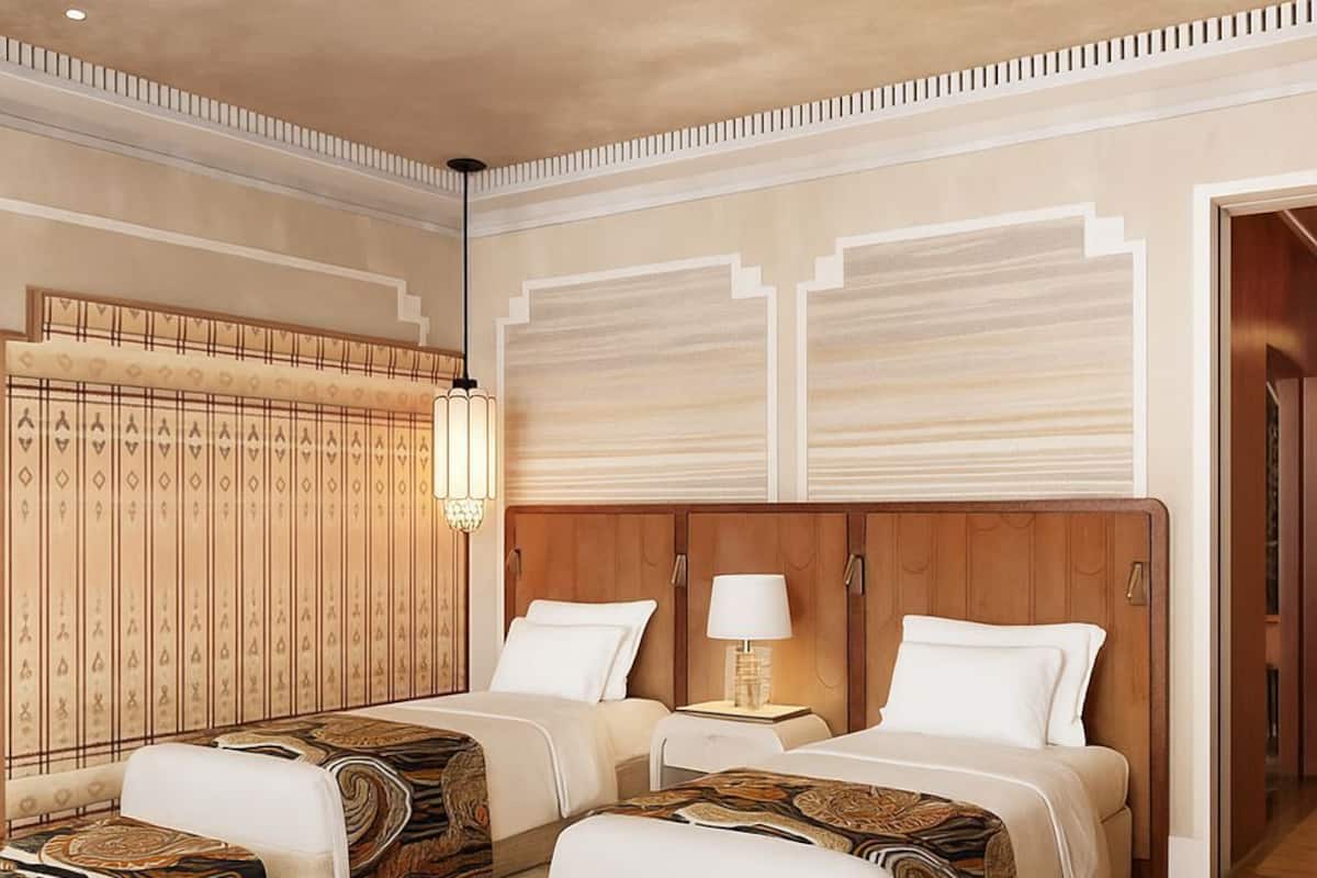 A hotel room with two beds, a wardrobe, a lamp, and a patterned rug.