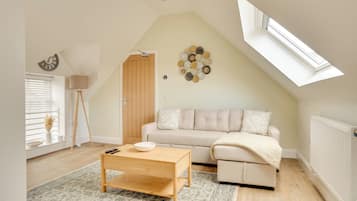 A cozy loft bedroom with a sloped ceiling, a large window, a beige sofa, and a wooden coffee table.