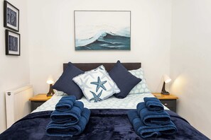 A neatly made bed with a dark blue blanket, two pillows with star patterns, and a framed artwork above.