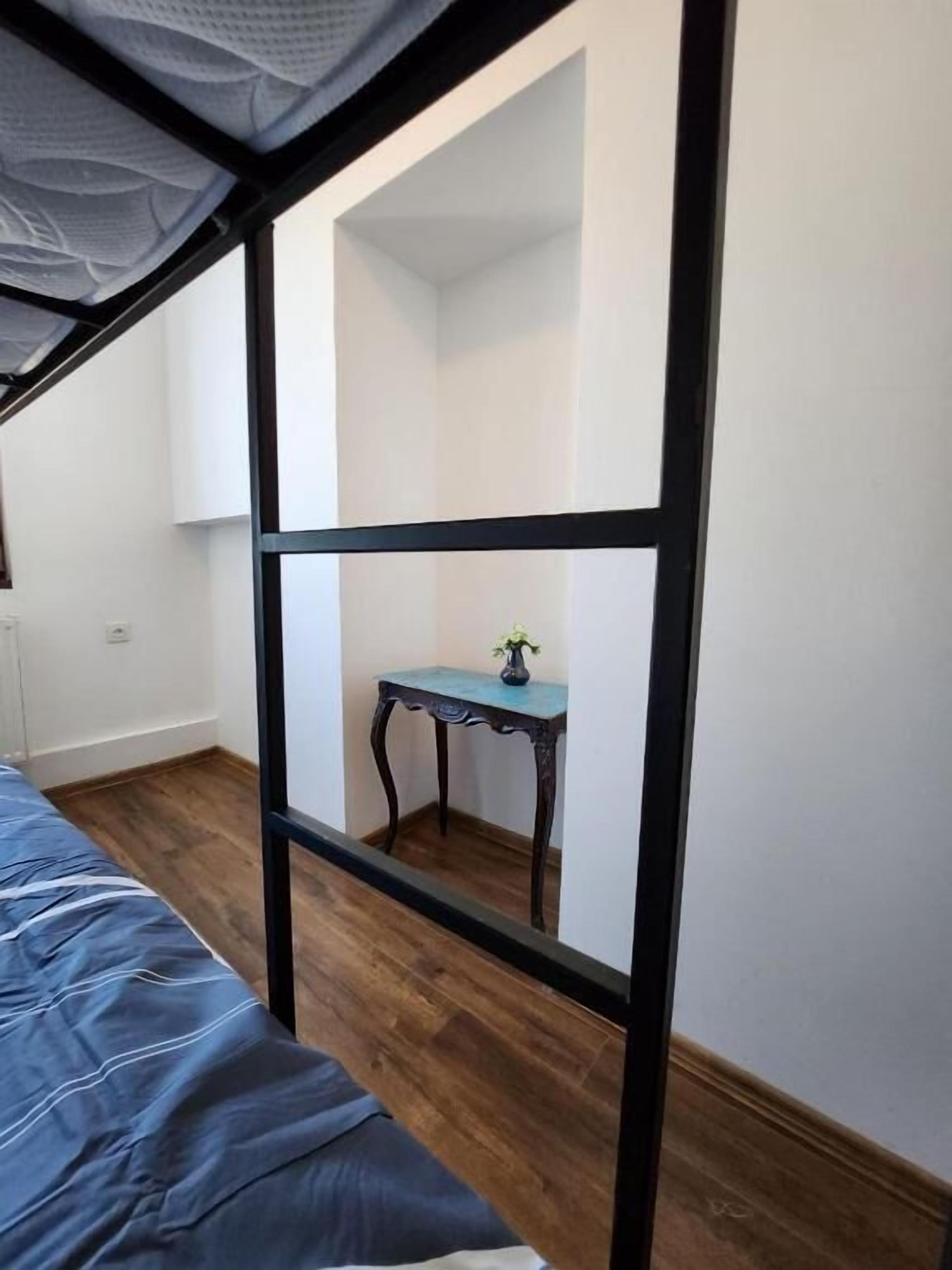 A room with a bunk bed, a small table with a vase, and a window with a white curtain.