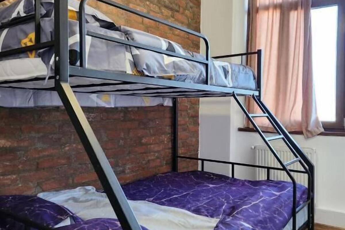 A bunk bed with a brick wall background, a window with curtains, and a radiator.
