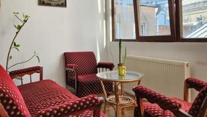 A cozy room with a wooden sofa, two armchairs, a small round table, and a window with a view of buildings and mountains. - City Guli  (Tbilisi)