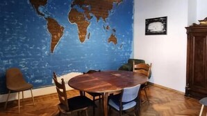 A dining area with a wooden herringbone floor, a round wooden table, and chairs. A large world map mural is on the wall, and a pendant light hangs above the table. - City Guli  (Tbilisi)