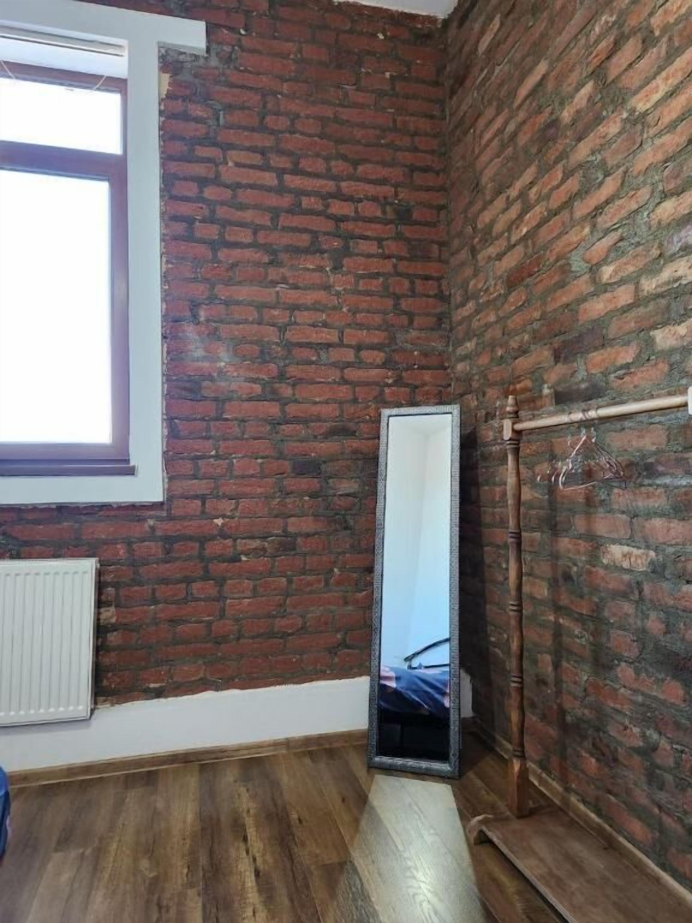 A room with a brick wall, a large window, a radiator, and a wooden floor.