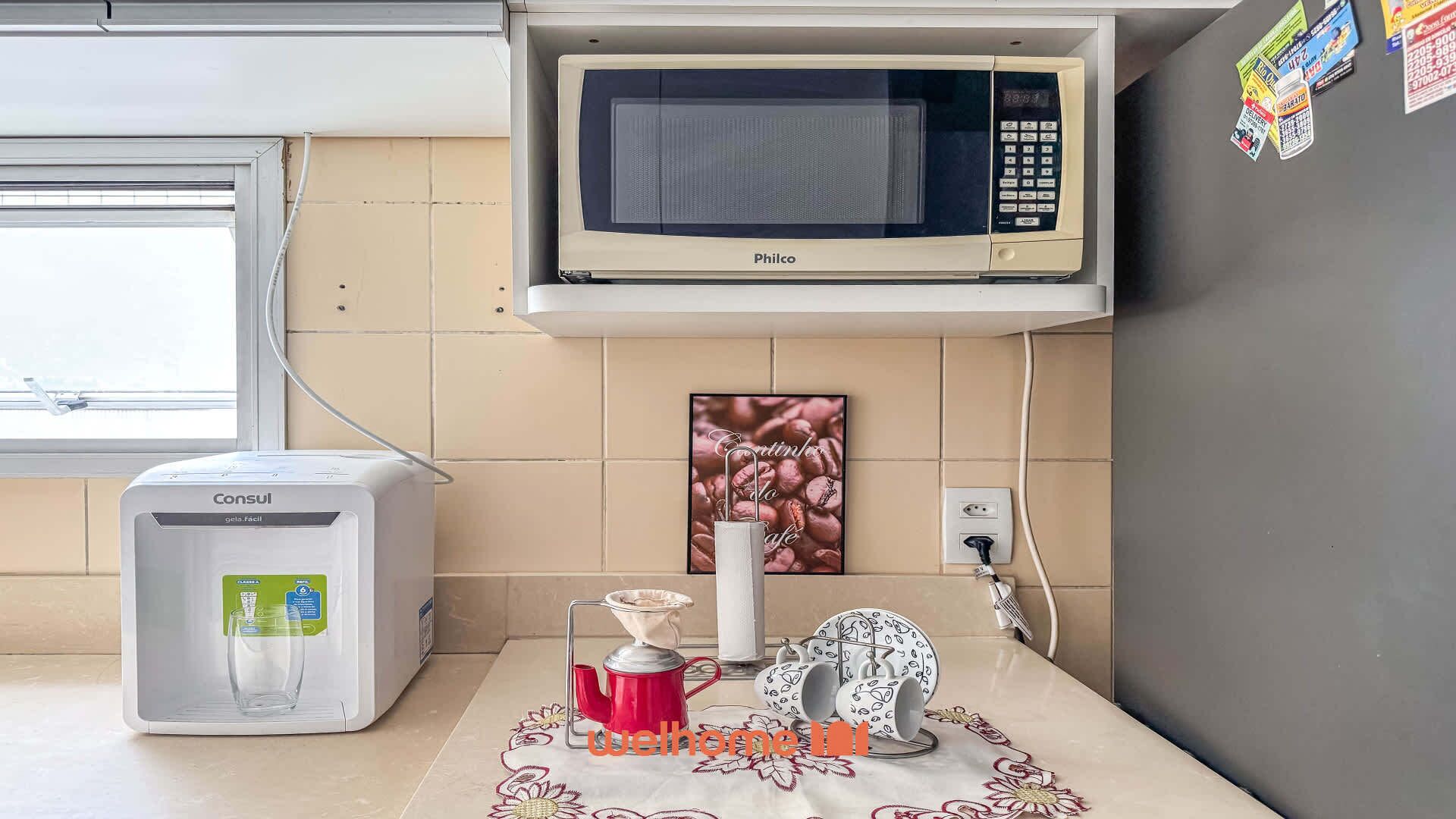Uma cozinha compacta com geladeira branca, cafeteira branca, micro-ondas e uma jarra de café no balcão.