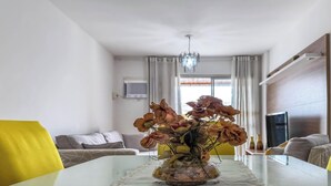 En matplats med ett glasbord, gula stolar, en vas med torkade blommor, en soffa och en tv i bakgrunden.