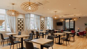 A modern dining area with wooden tables and chairs, large windows with curtains, and decorative hanging lights.