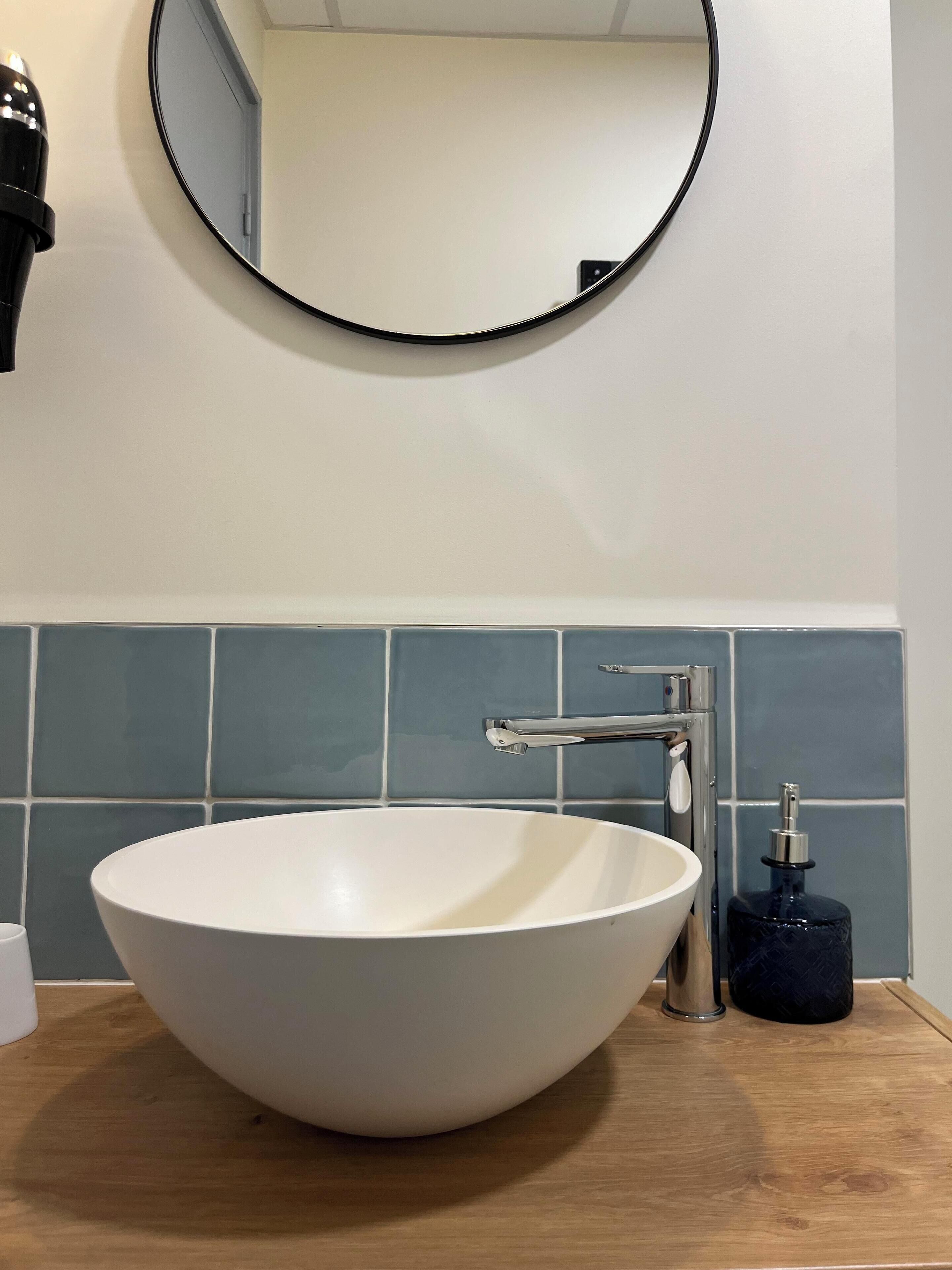 A bathroom with a white sink, a round mirror, and a blue-tiled wall.