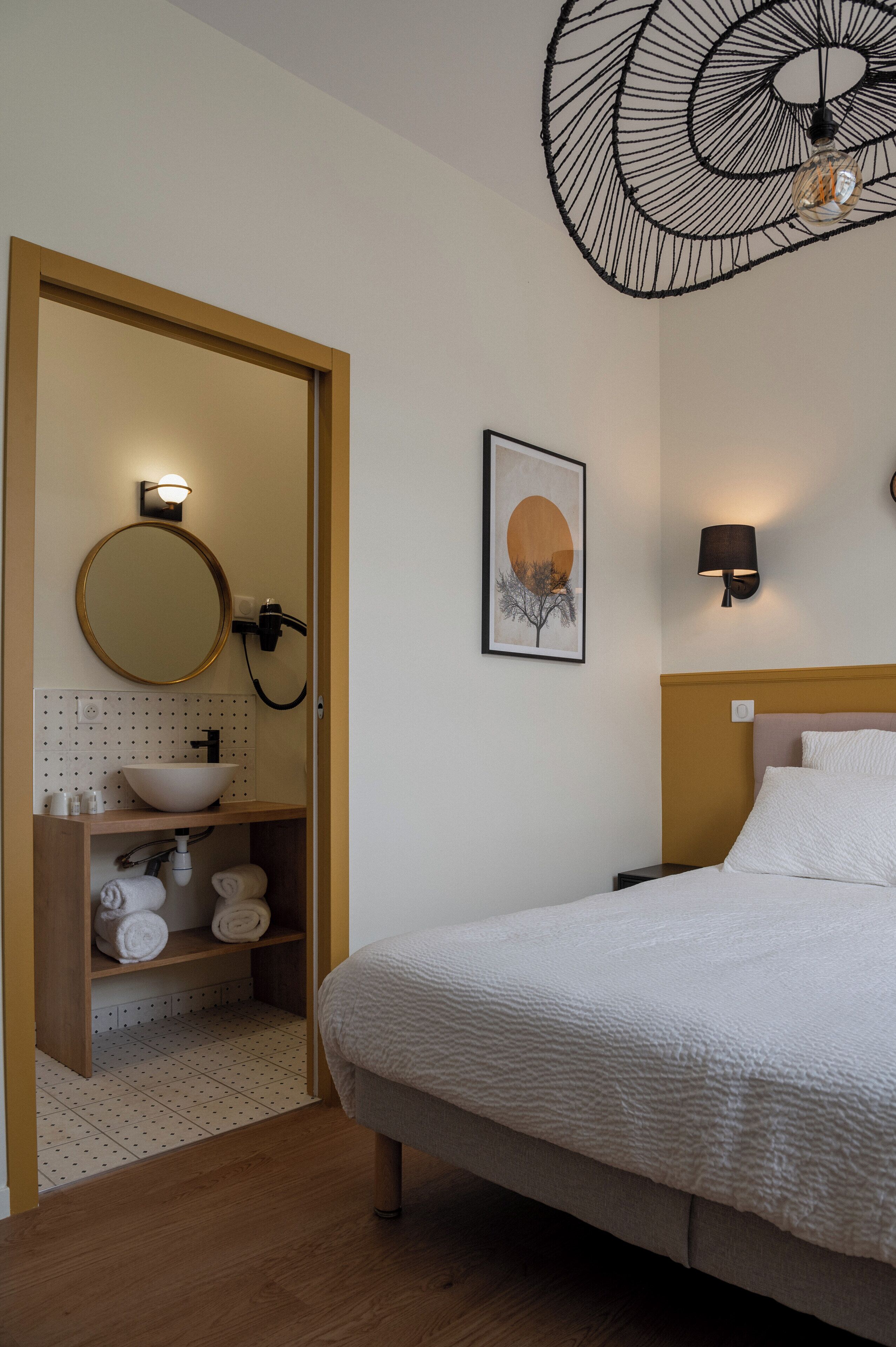 A bedroom with a bed, a bathroom with a sink, and a wall-mounted light fixture.