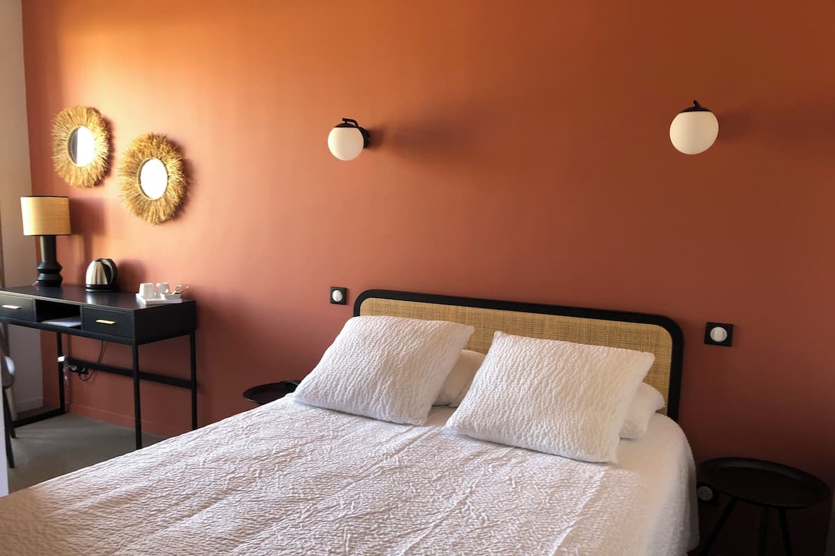 Una cama bien hecha con sábanas blancas, un escritorio con lámpara y dos luces fijadas a la pared.