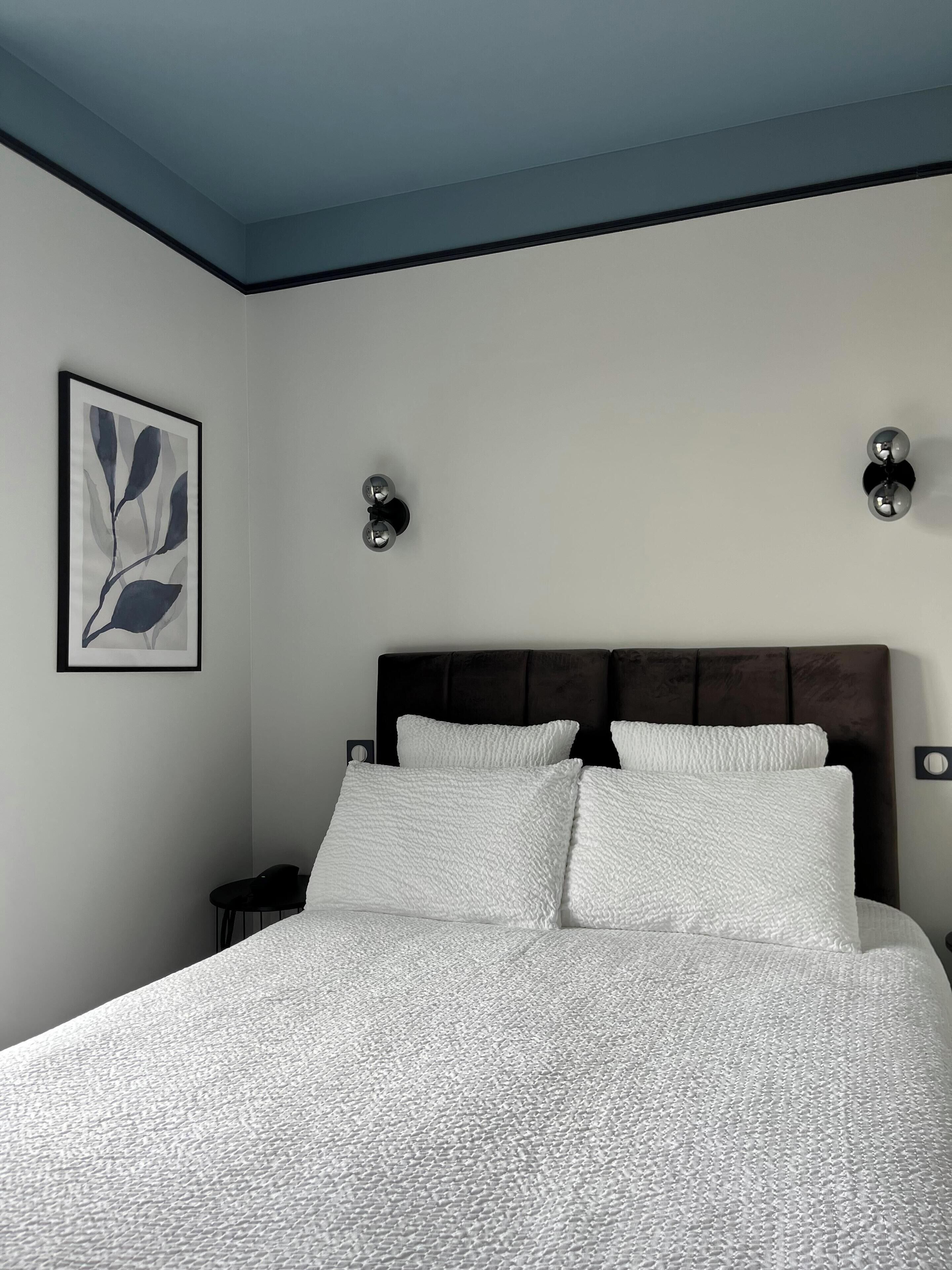 A bedroom with a bed, a nightstand, a wall-mounted lamp, and a framed artwork.