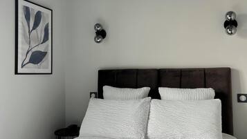 A bedroom with a bed, a nightstand, a wall-mounted lamp, and a framed artwork.