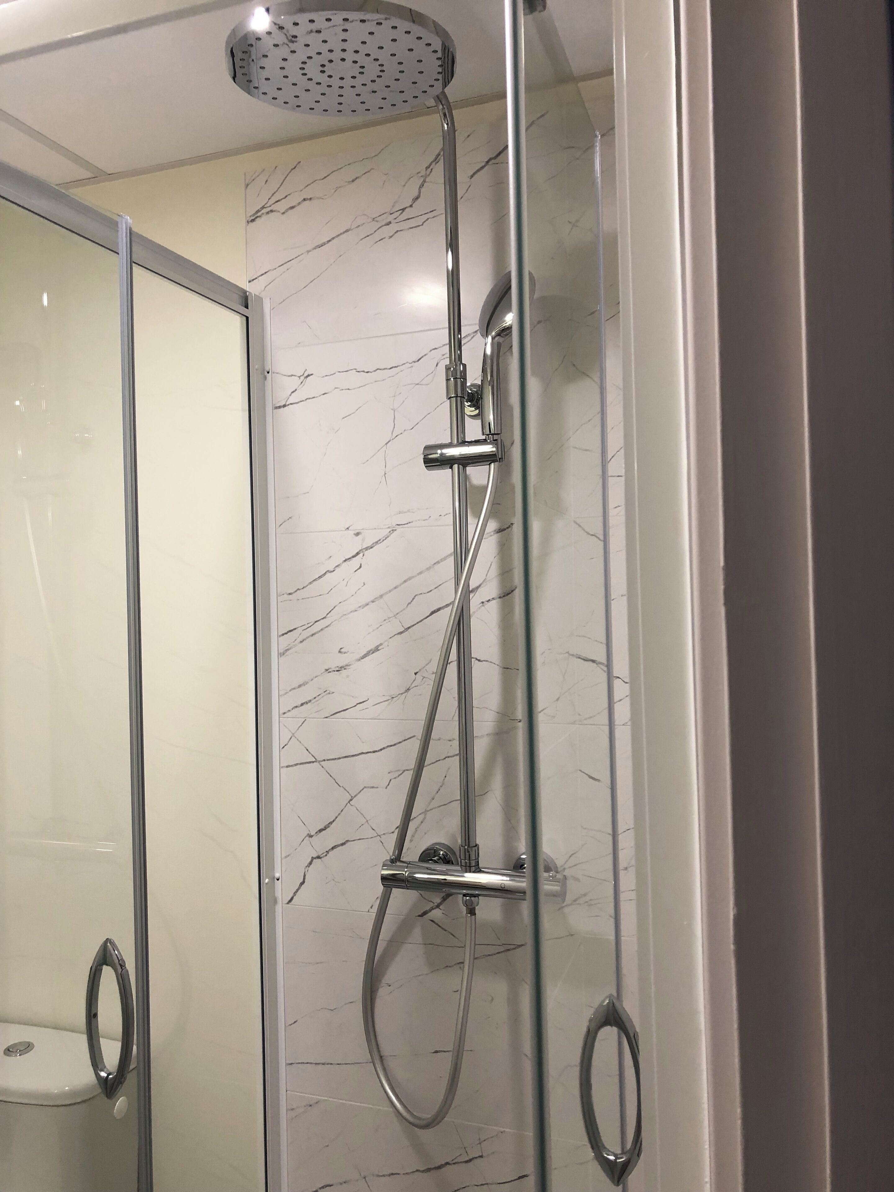 Ducha moderna con cabezal de ducha de mano y grifo empotrado, frente a una pared de mármol.