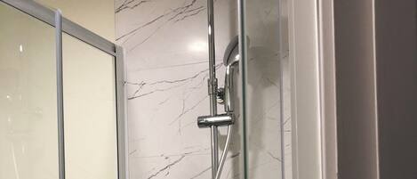 Ducha moderna con cabezal de ducha de mano y grifo empotrado, frente a una pared de mármol.