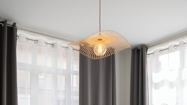 A bedroom with a bed, a green armchair, a hanging light fixture, and sheer curtains.