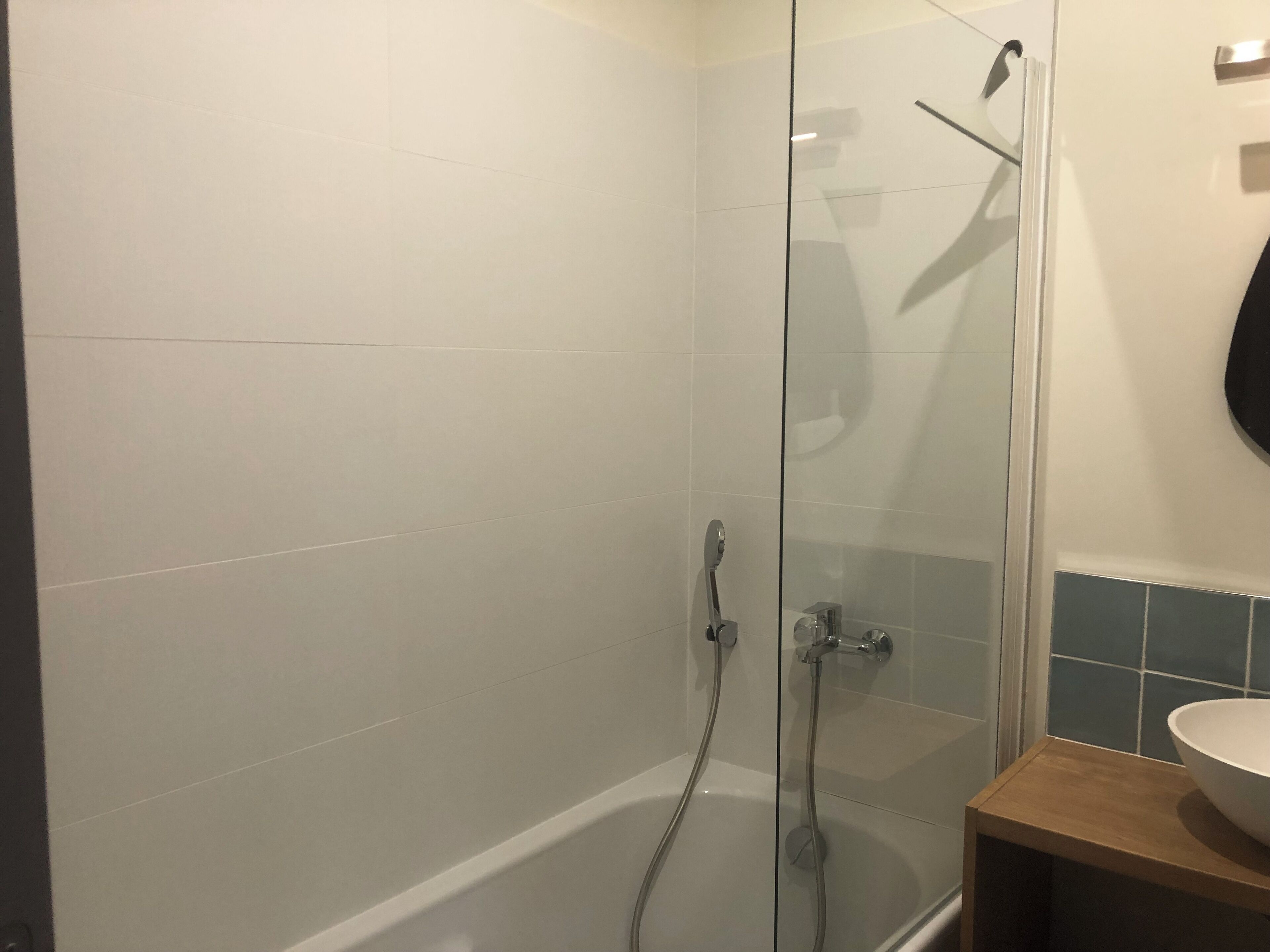 Un baño moderno con ducha envuelta en cristal, una bañera y un mueble de tocador de madera con lavamanos blanco.