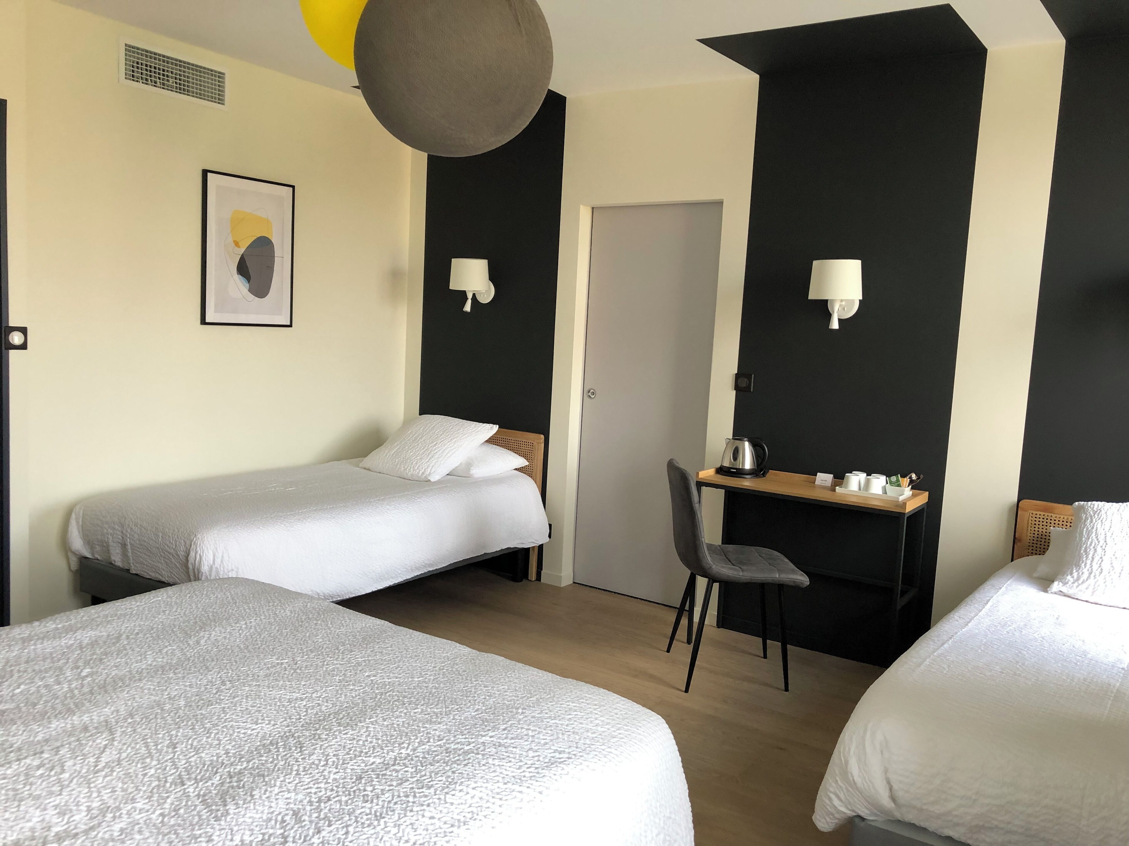 A hotel room with two beds, a desk, a chair, and a door.