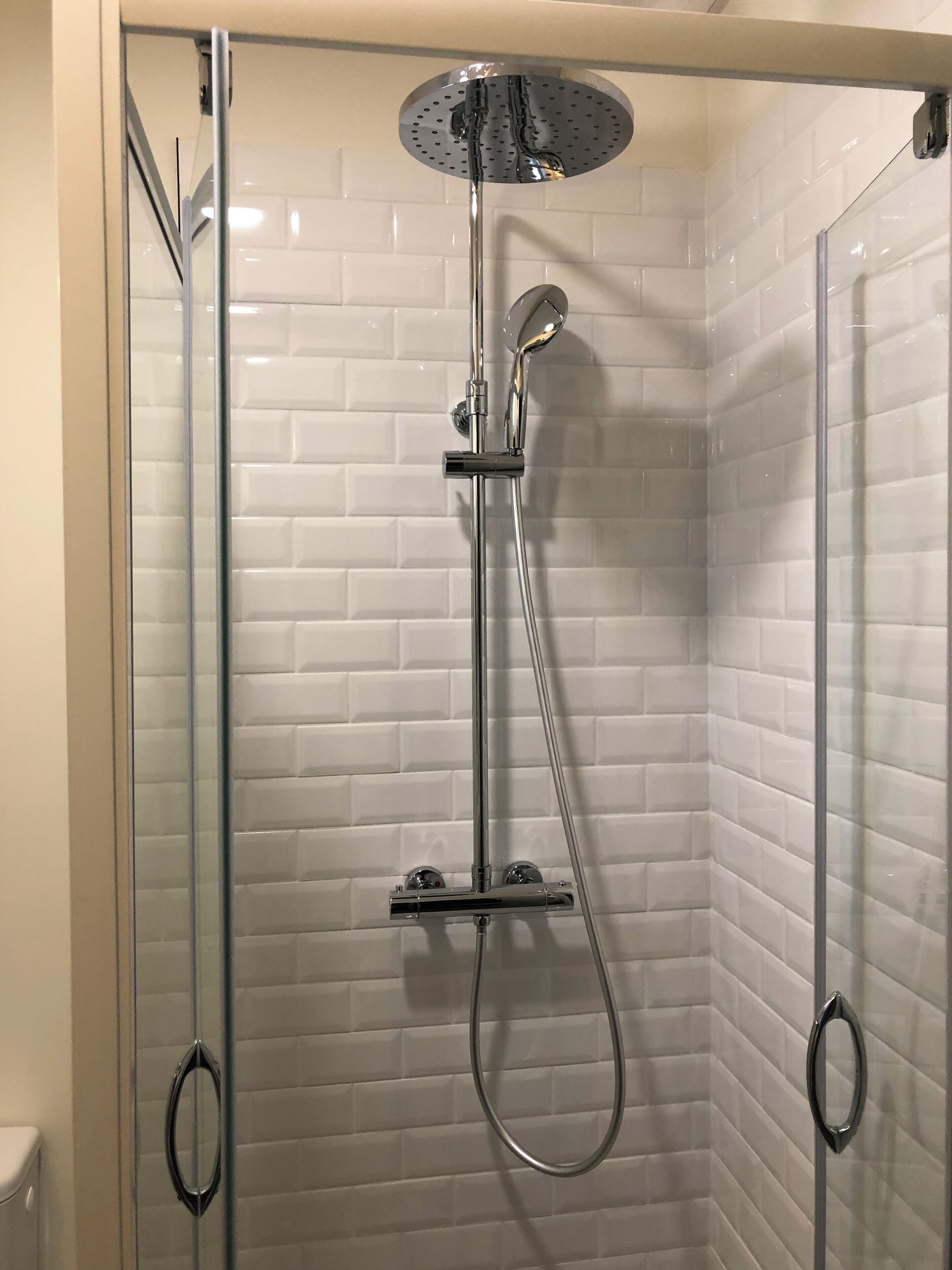 A glass-enclosed shower with a handheld showerhead and a fixed overhead rain showerhead.