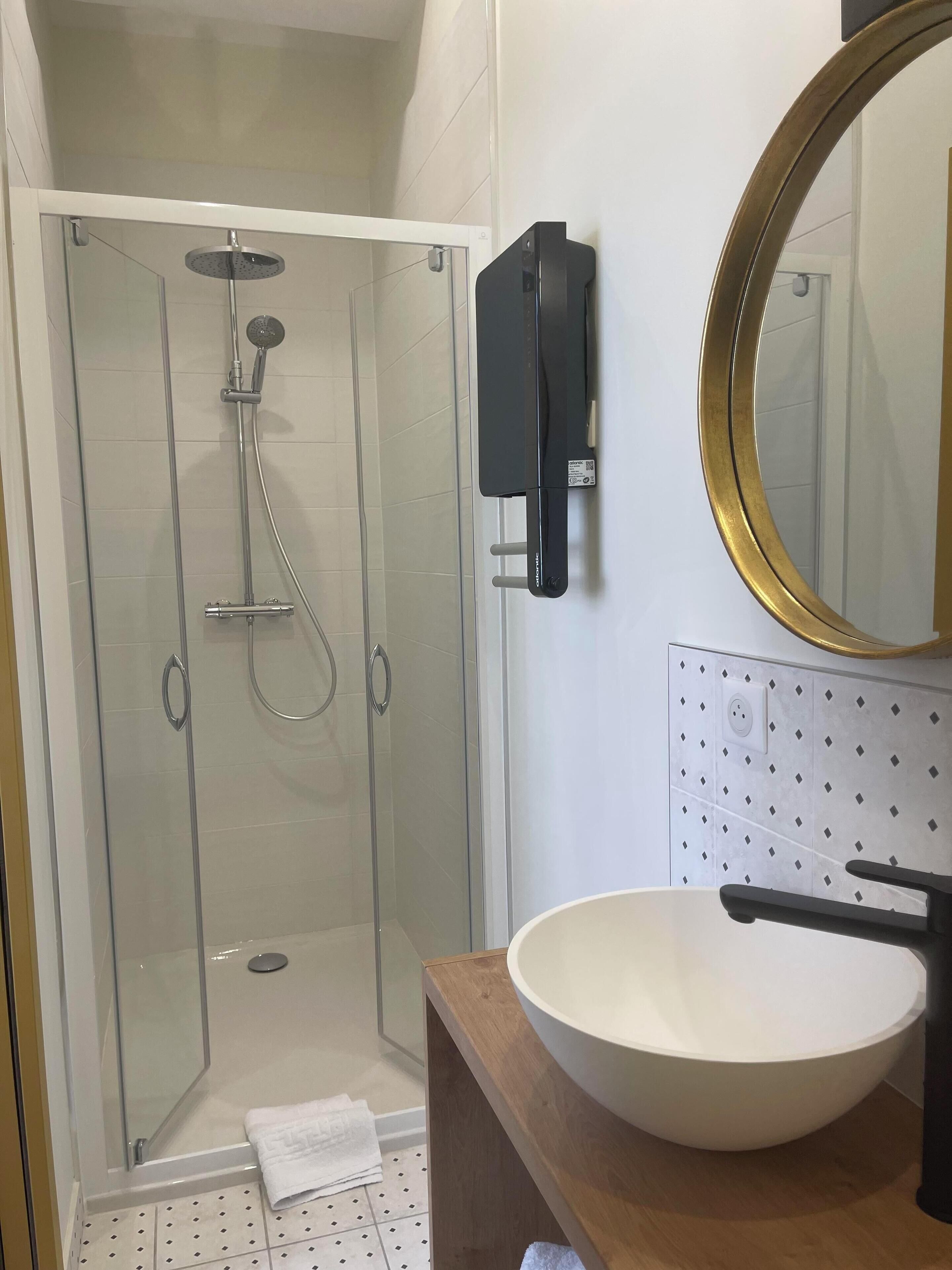 Un baño moderno con ducha de vidrio, lavamanos con tocador de madera y espejo montado en la pared.